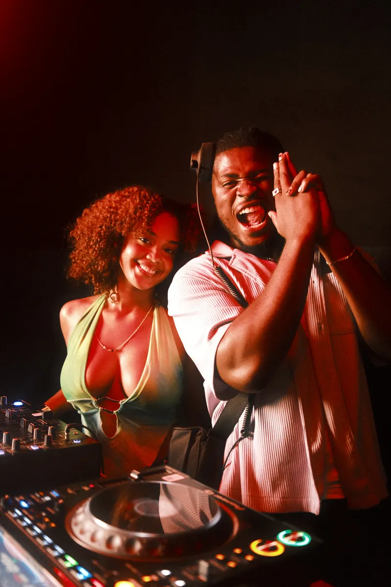 Two friends laughing behind a DJ booth in red light