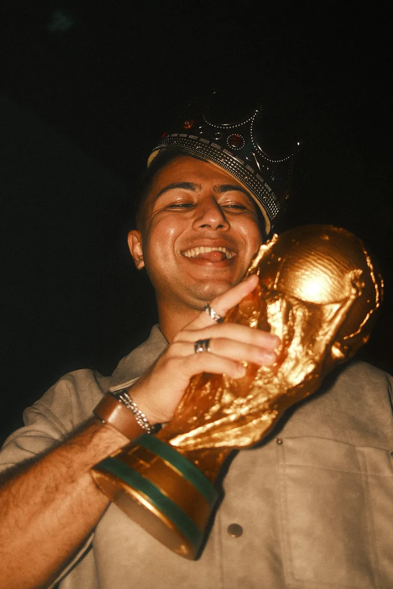 A friend in a gold crown laughs with his eyes closed, hugging a gold trophy to his cheek