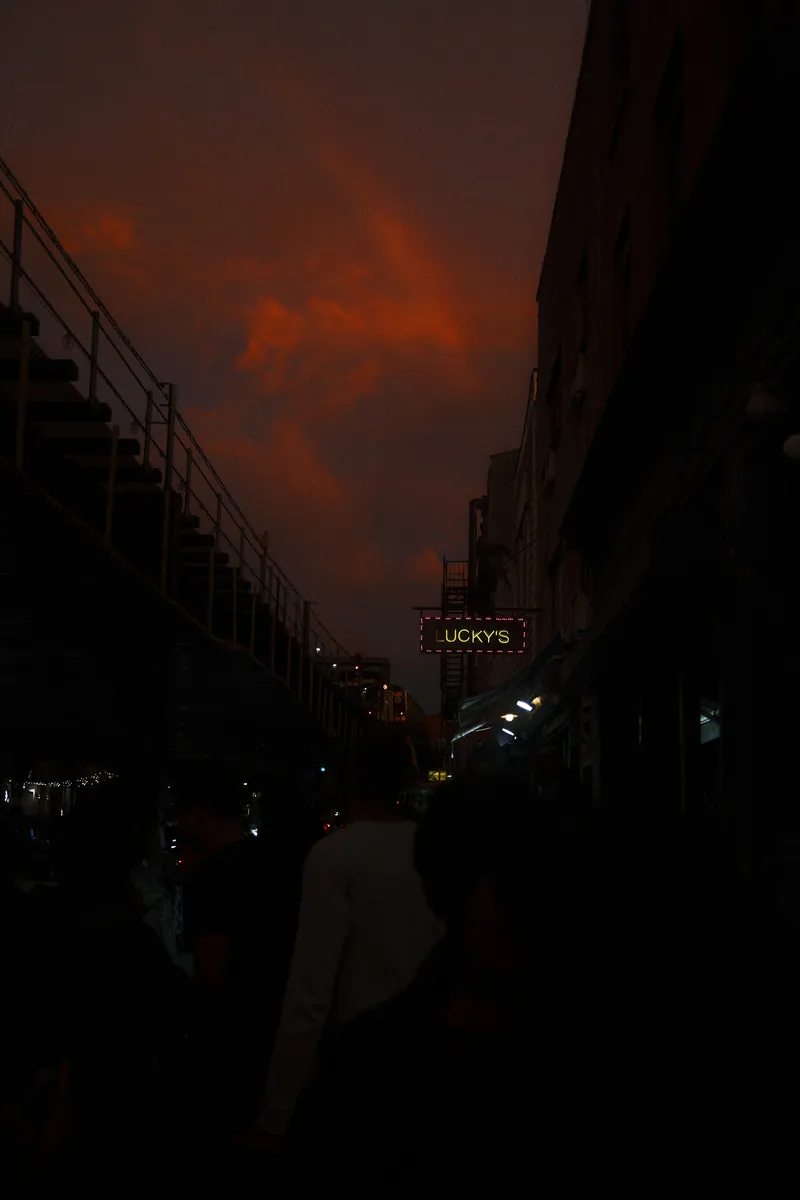 A red storm sky over an elevated train line, with a glowing Lucky’s sign below