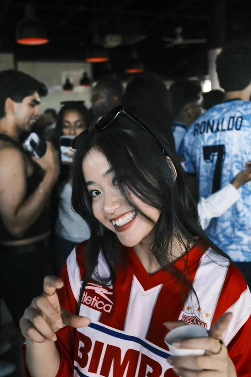 A friend in a red striped soccer jersey grinning at a crowded watch party