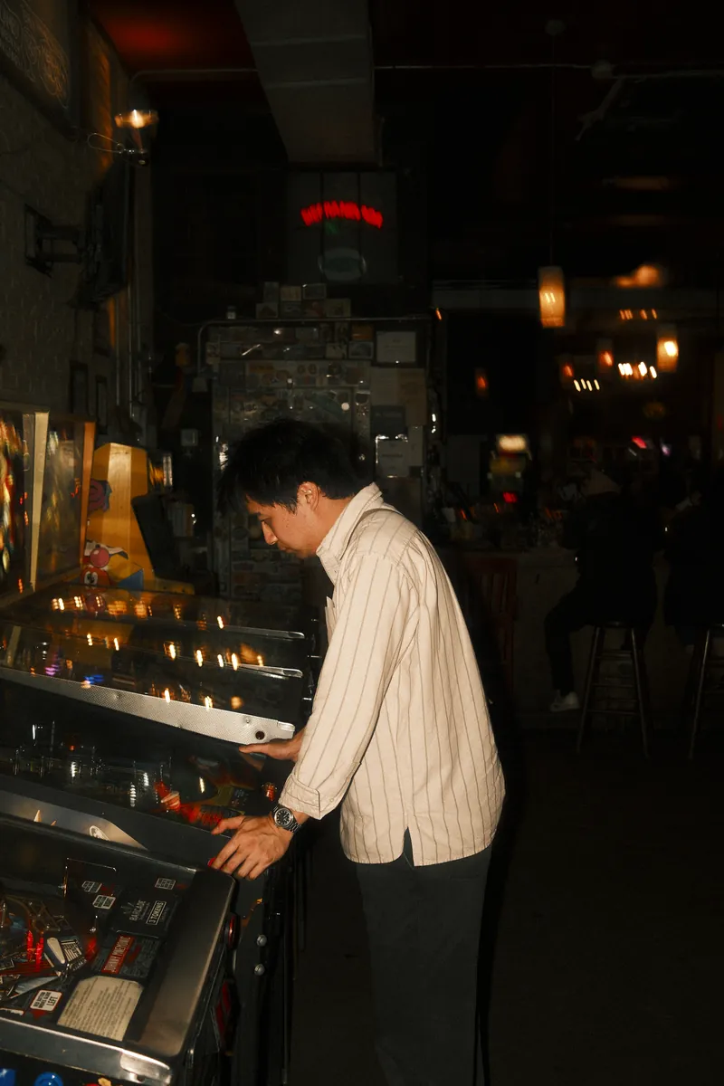A friend in a striped shirt leaning into a pinball machine at an arcade bar