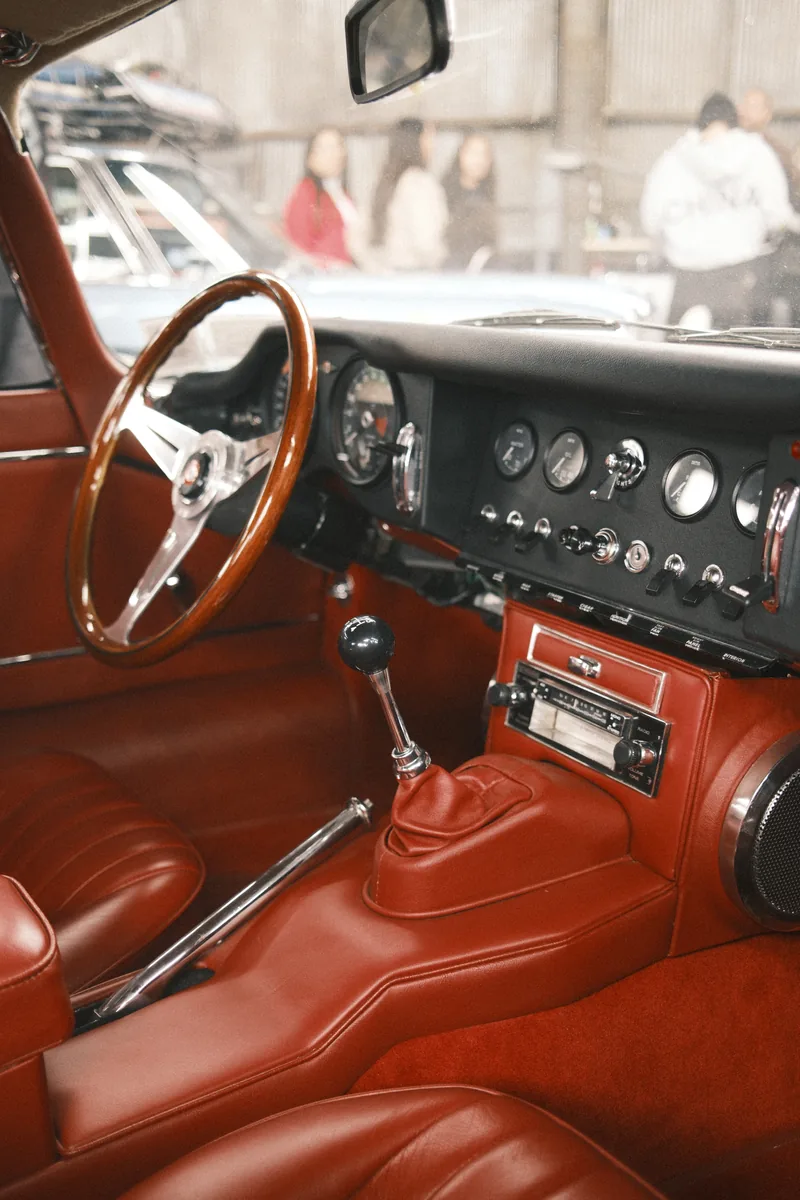 The red leather interior of a vintage sports car, wooden steering wheel and chrome dials