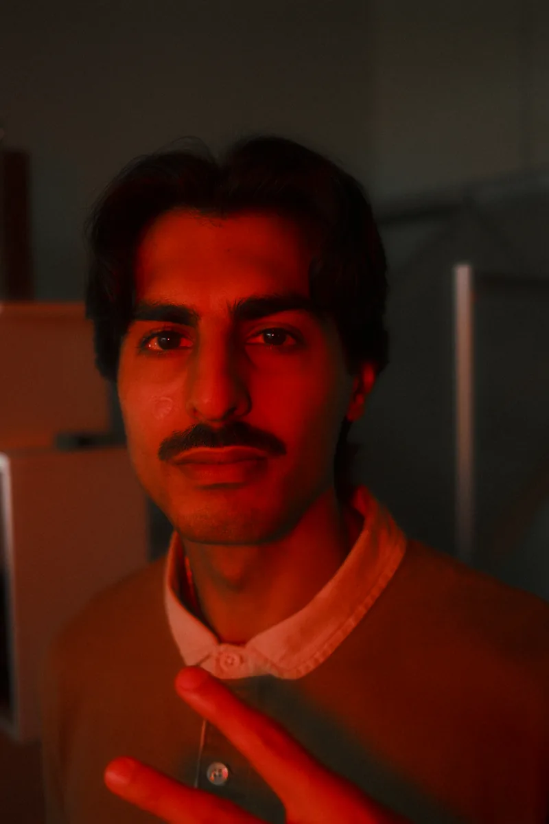A man with a thin mustache looks into the camera, his face lit deep red