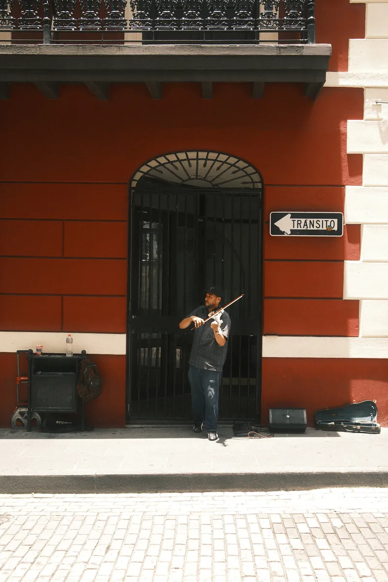 A street violinist in an arched doorway on a red wall with a Tránsito sign